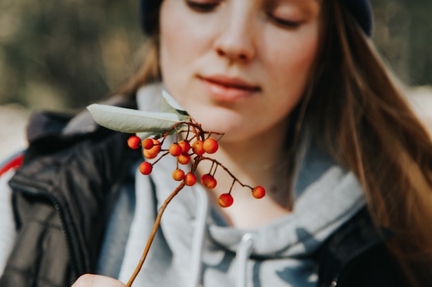 Primo piano di una giovane ragazza caucasica in possesso di un ramoscello con frutti di bosco in mano. Trekking nel concetto di foresta.