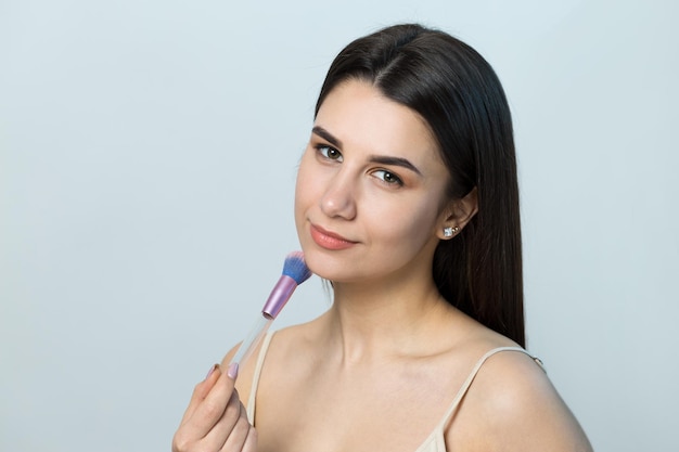 Primo piano di una giovane ragazza in un top leggero su uno sfondo bianco che fa un trucco facciale