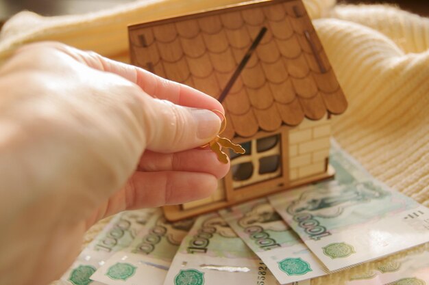 Primo piano di una mano che tiene le chiavi e un modello di una casa di legno su una sciarpa calda con soldi