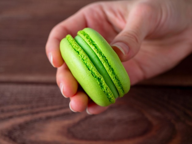 Primo piano di una mano che tiene un biscotto di mandorla verde su uno sfondo di legno Delizioso dessert francese