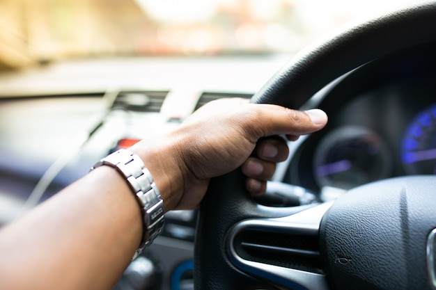 Primo piano di una mano dell'uomo che conduce un'automobile con il giorno soleggiato.