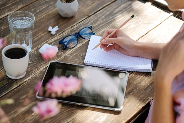 Primo piano di una mano di una donna d'affari che lavora su una tavoletta digitale e scrive appunti bevendo caffè