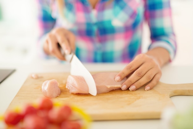 Primo piano di una mano femminile che taglia il filetto di pollo sul bordo della cucina.