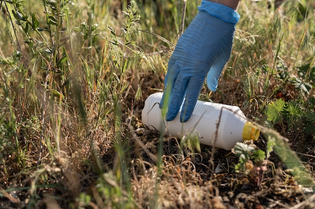 Primo piano di una mano femminile in un guanto di gomma. I volontari raccolgono la spazzatura nel parco. Rifiuti di plastica. Inquinamento ambientale