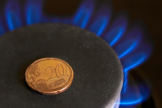 Primo piano di una moneta da 20 centesimi sul fornello a gas con fiamma come concetto di aumento del prezzo del gas naturale