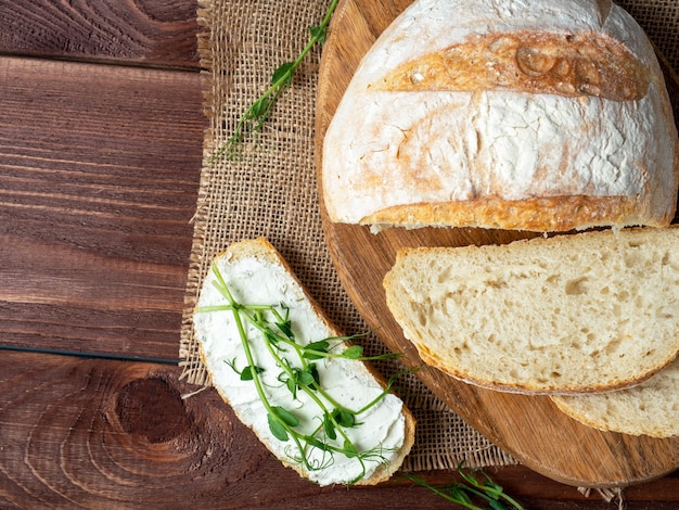 Primo piano di una natura morta fatta di pane fresco croccante Una fetta di pane spalmata di ricotta e decorata con micro vegetazione Tovagliolo di lino marrone sullo sfondo di legno vista dall'alto laici piatta