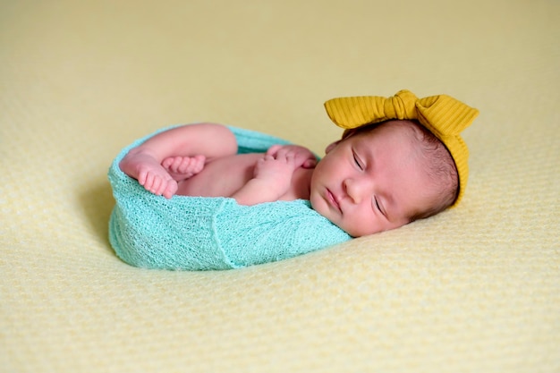 Primo piano di una neonata all'interno di un gomitolo di lana blu su una coperta gialla con un fiocco giallo sulla testa