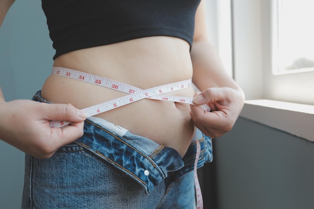 Primo piano di una pancia con cicatrice da taglio e grasso addominale Salute delle donne Una donna vestita con abiti sportivi che dimostra il suo corpo imperfetto dopo un parto con la scuola materna sullo sfondo