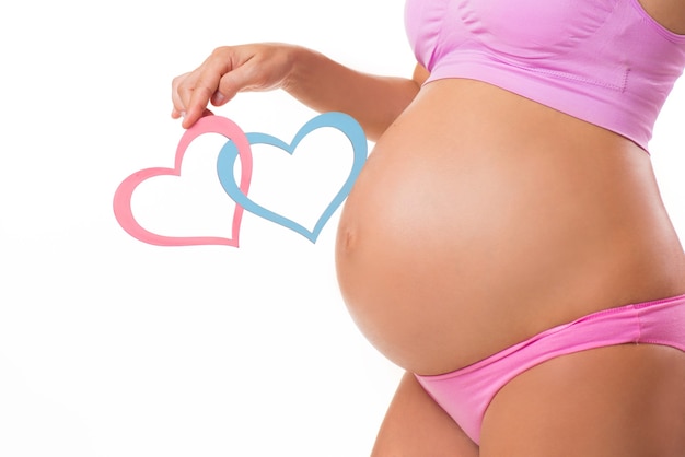 Primo piano di una pancia incinta con cuori rosa e blu Indovina il sesso della bambina o dei gemelli