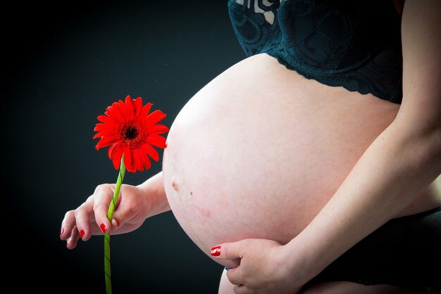 Primo piano di una pancia incinta con un fiore di gerbera rosso su sfondo nero