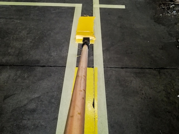 Primo piano di una persona che dipinge una linea gialla sul pavimento di un garage sotto le luci