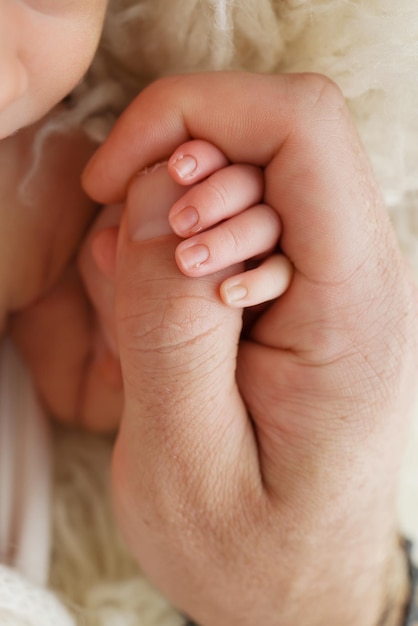 Primo piano di una piccola mano di un bambino e della mano di madre e padre Un neonato dopo la nascita tiene stretto il pollice dei suoi genitori