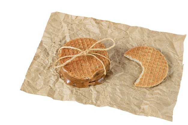 Primo piano di una pila di stroopwafel su una carta marrone accanto a un altro biscotto con uno sfondo morso bianco