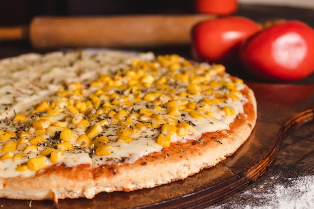 Primo piano di una pizza di mais e mozzarella con pomodoro su un tavolo di legno.