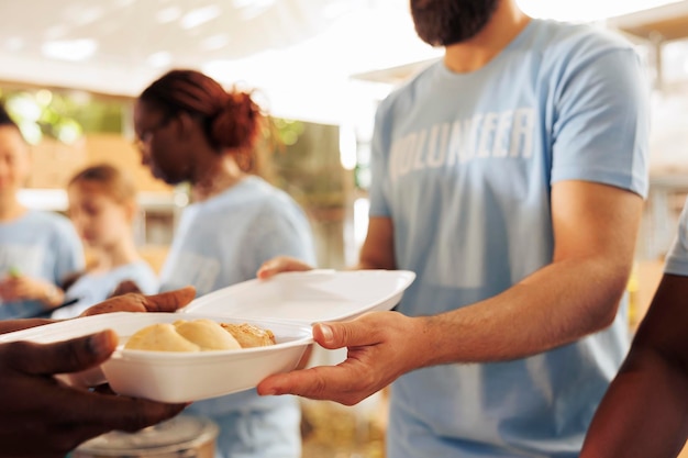 Primo piano di una scatola di pasti freschi, all'aperto, servita ai meno fortunati, combattendo la fame e la povertà. Immagine dettagliata di un volontario maschio caucasico che distribuisce cibo gratuito in un rifugio per senzatetto.