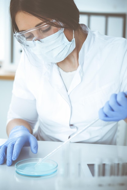 Primo piano di una scienziata professionista in occhiali protettivi che fa esperimenti con reagenti o analisi del sangue in laboratorio. Medicina, biotecnologia e concetto di ricerca.