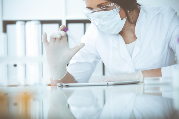 Primo piano di una scienziata professionista in occhiali protettivi che fa esperimenti con reagenti o analisi del sangue in laboratorio. Medicina, biotecnologia e concetto di ricerca.