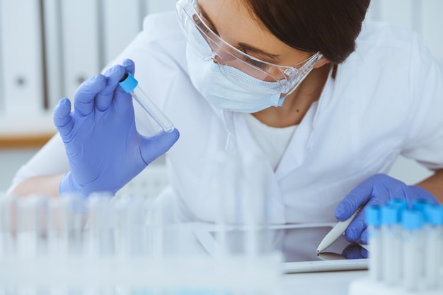 Primo piano di una scienziata professionista in occhiali protettivi che fa esperimenti con reagenti o analisi del sangue in laboratorio. Medicina, biotecnologia e concetto di ricerca.