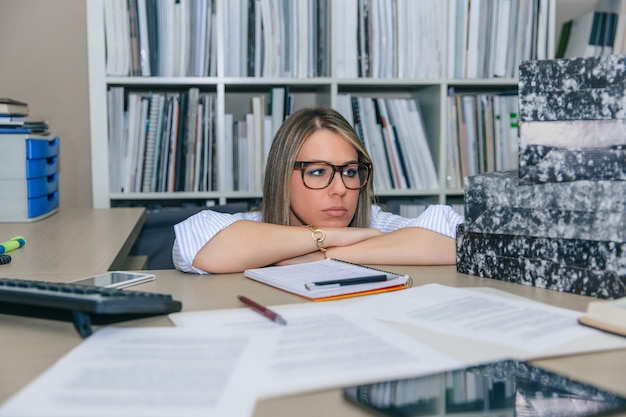 Primo piano di una segretaria bionda esausta che guarda la pila di cartelle in attesa di essere archiviata nel suo desktop