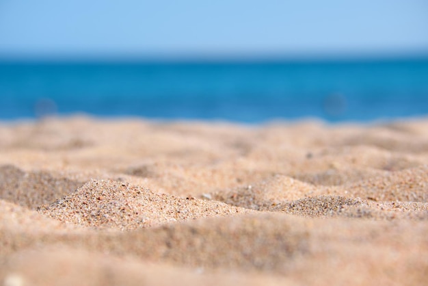 Primo piano di una superficie di sabbia gialla pulita che copre la spiaggia di mare con acqua di mare blu sullo sfondo. Concetto di viaggi e vacanze.