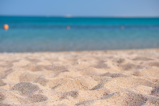 Primo piano di una superficie di sabbia gialla pulita che copre la spiaggia di mare con acqua di mare blu sullo sfondo. Concetto di viaggi e vacanze.