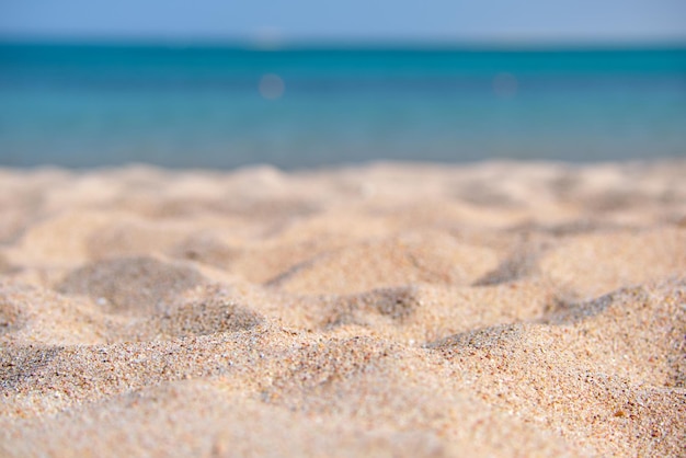 Primo piano di una superficie di sabbia gialla pulita che copre la spiaggia di mare con acqua di mare blu sullo sfondo. Concetto di viaggi e vacanze.