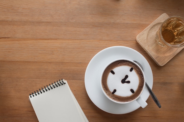 Primo piano di una tazza calda caffè latte arte disegnato un concetto di business oclock sul tavolo di legno con il libro di nota