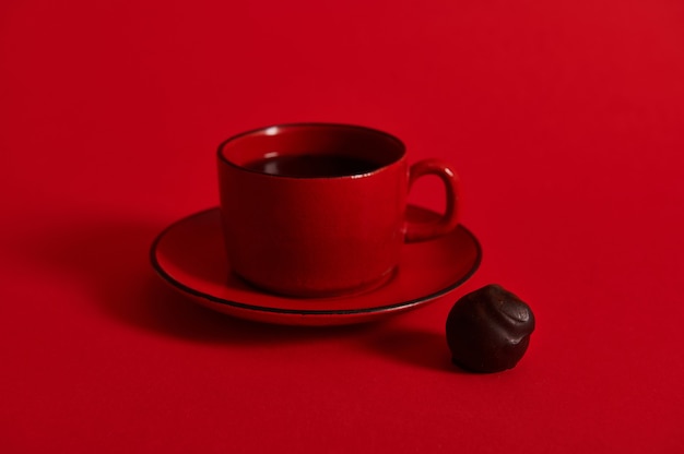 Primo piano di una tazza di caffè in ceramica rossa su un piattino e un tartufo di cioccolato sulla superficie rossa.