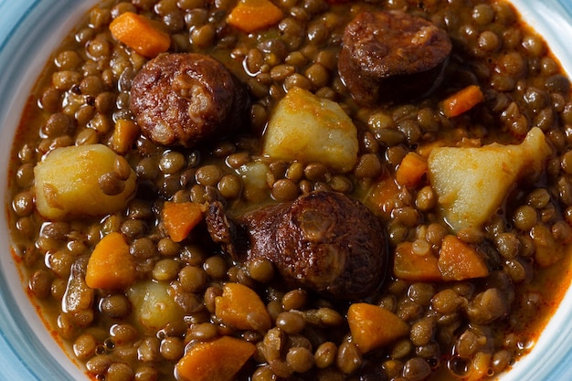 Primo piano di una tradizionale zuppa di lenticchie con gambe, carote e chorizo. Cucina mediterranea