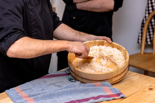Primo piano di uno chef di sushi professionista che prepara il riso in una ciotola di legno
