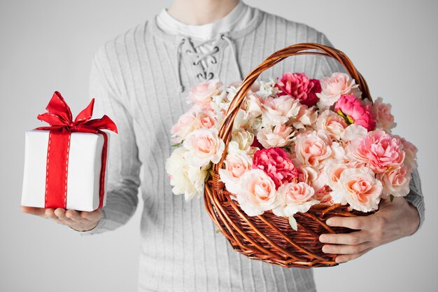 primo piano di uomo che tiene cesto pieno di fiori e confezione regalo.