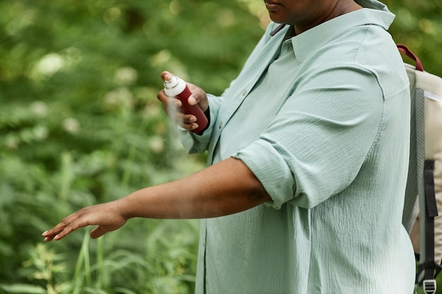 Primo piano di vista laterale della donna di colore che spruzza armi con repellente per insetti all'aperto