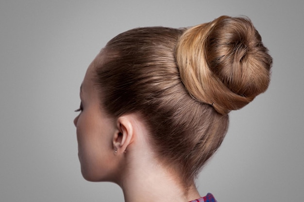 Primo piano di vista laterale di profilo della donna con i capelli raccolti marroni eleganti creativi del panino dell'acconciatura