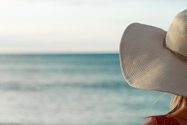 Primo piano di vista posteriore della donna che indossa un cappello che guarda verso l'oceano blu