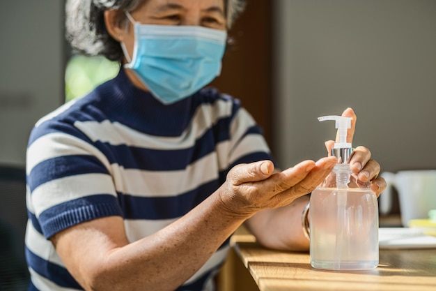 Primo piano donna asiatica anziana che usa disinfettante per le mani pompando gel alcolico e lavando prima di lavorare