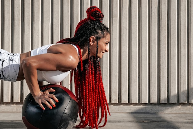 Primo piano Donna atletica che fa esercizio con palla medica Forza e motivazioneFoto di donna sportiva in abbigliamento sportivo alla moda