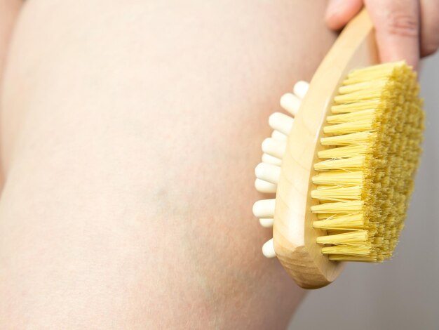 Primo piano Donna che fa massaggio alle gambe con una spazzola di massaggio morbida in legno per corpo e gambe Cura della pelle per la prevenzione della cellulite