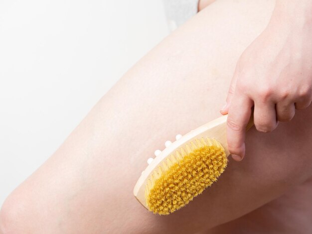 Primo piano Donna che fa massaggio alle gambe con una spazzola di massaggio morbida in legno per corpo e gambe Cura della pelle per la prevenzione della cellulite