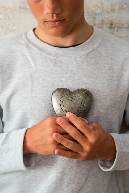 Primo piano e ritratto di adolescente o millenario che tiene un cuore di metallo - uomo sano