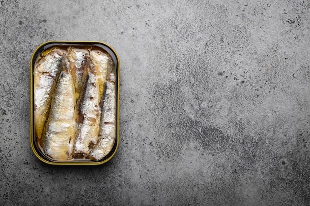 Primo piano e vista dall'alto di sardine in scatola in una latta su sfondo grigio cemento, spazio per il testo. Pesce in scatola come alimento conveniente, veloce, sano e fonte di acidi grassi omega-3, proteine e vitamina D