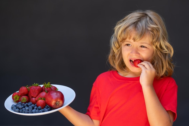 Primo piano estate ritratto di capretto con piatto di frutti estivi mix Sano frutta fragola organica stagione estiva Kid mangiare fragola matura