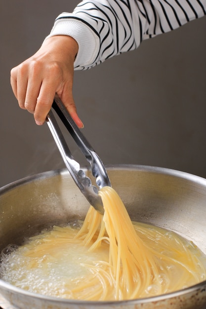 Primo piano Estrarre gli spaghetti bolliti dalla padella con pinze in acciaio inossidabile, processo di cottura in cucina