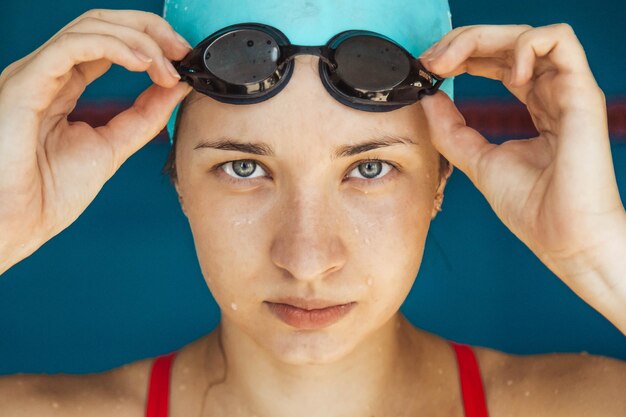 Primo piano estremo di una testa di ragazza caucasica con una cuffia da nuoto e le mani che mettono gli occhialini da nuoto che si preparano per l'allenamento in piscina