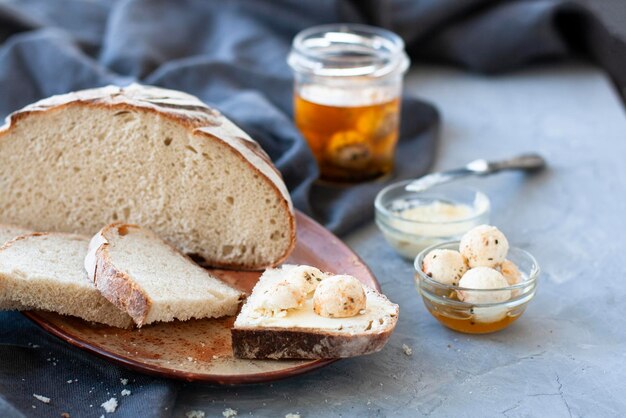 Primo piano fette di pane fatto in casa con burro, coltello e vaso aperto su sfondo grigio sfocato