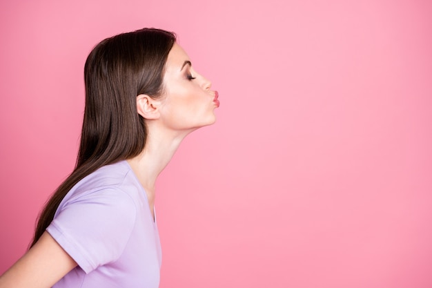 Primo piano foto del profilo di bella civettuola attraente signora lunga pettinatura affascinante inviare baci aria spazio vuoto occhi chiusi data indossare casual t-shirt viola isolato sfondo rosa colore pastello