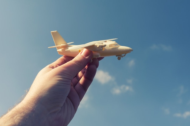 Primo piano foto di mano maschio che tiene aeroplano giocattolo contro il cielo blu