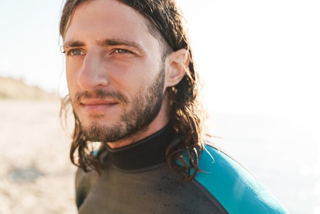 Primo piano fotografico di un bell'uomo serio in muta che guarda da parte mentre si allena sulla spiaggia soleggiata