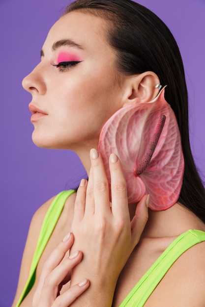 Primo piano fotografico di una donna seducente caucasica con un trucco luminoso che tiene in mano un fiore esotico