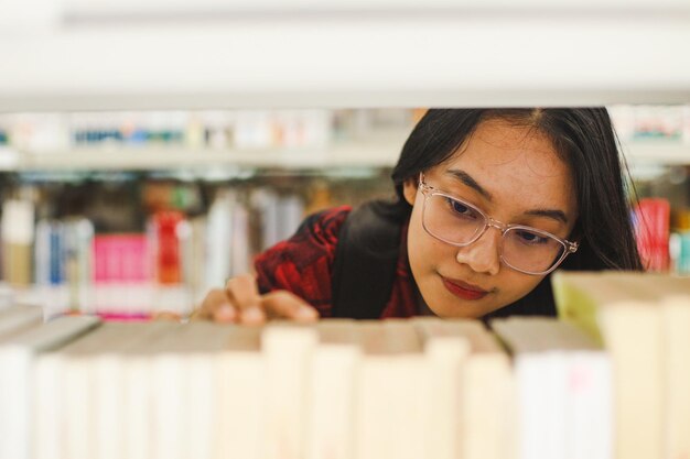 Primo piano giovane donna asiatica che passa in rassegna i libri alla ricerca del libro necessario da leggere in biblioteca