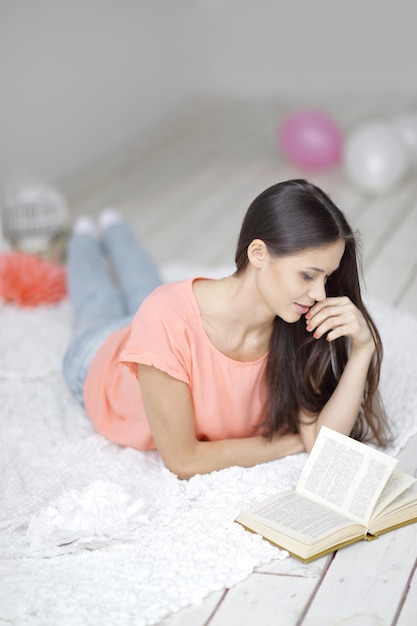 Primo piano.giovane donna che legge un libro sdraiata sul pavimento in soggiorno